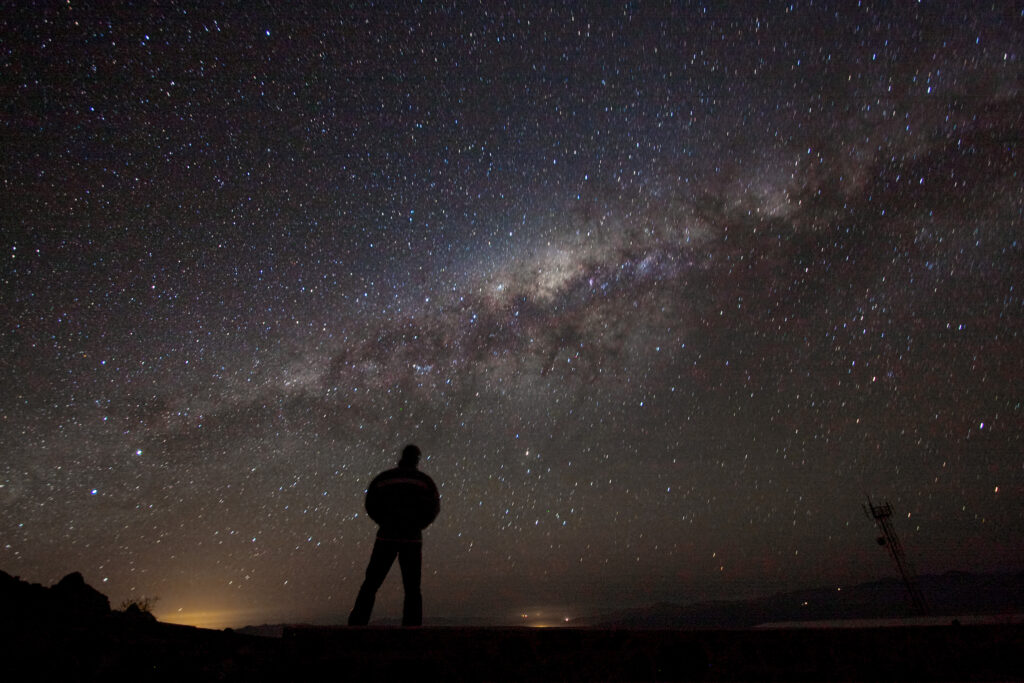 A lone observer gazing up at the Milky Way, symbolising consciousness meeting the cosmos