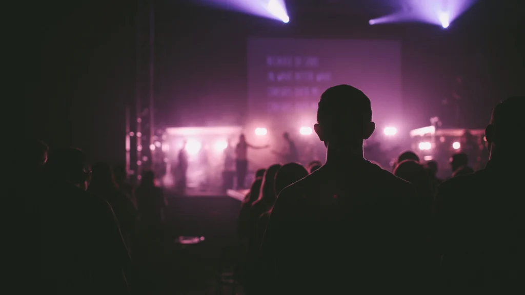 Audience silhouettes facing a stage lit with purple light and haze, the typical setting of so-called group meditations at large events