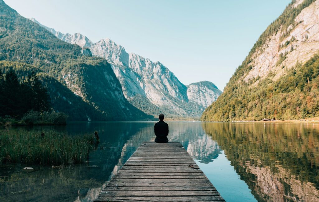 Une personne assise en silence sur le ponton d'un lac de montagne