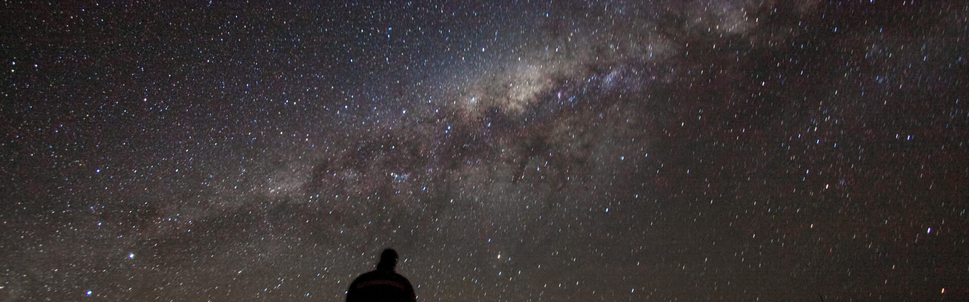 A lone observer gazing up at the Milky Way, symbolising consciousness meeting the cosmos
