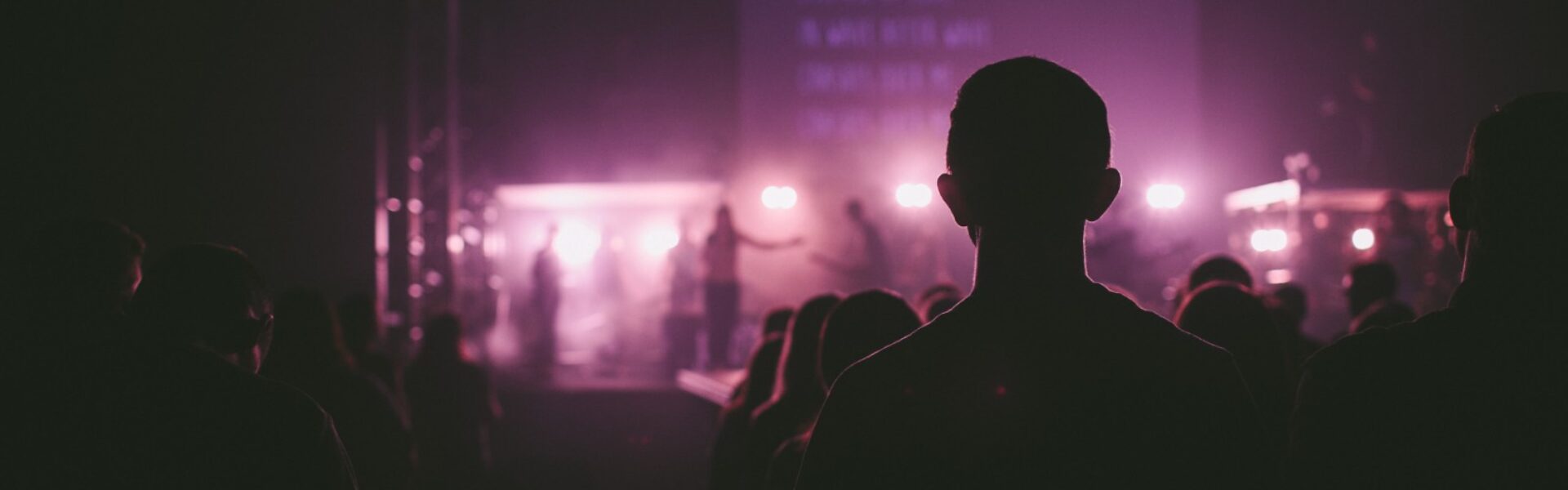 Audience silhouettes facing a stage lit with purple light and haze, the typical setting of so-called group meditations at large events